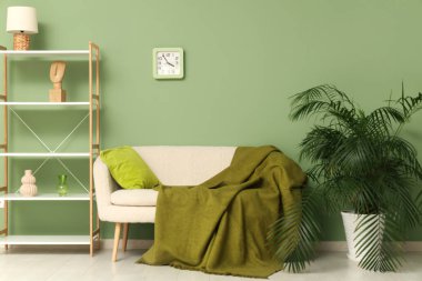 Oturma odasının içinde beyaz kanepe, raf ünitesi ve saat yeşil duvarda.