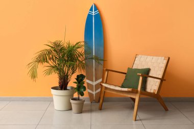 Sarı duvarın yanında bitki ve koltuk olan sörf tahtası.
