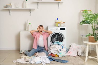 Çamaşır makinesinin yanında kirli çamaşırlarıyla şok olmuş genç bir kadın.