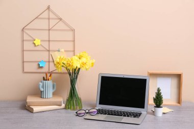 Kitaplı şık bir iş yeri, bir buket narsist çiçek ve ofiste bej duvarın yanında dizüstü bilgisayar.