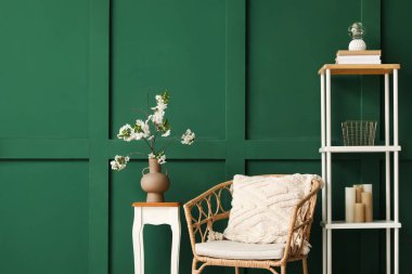 Yeşil oturma odasındaki rahat koltuğun yanındaki sehpanın üzerinde çiçek açan bir vazo.