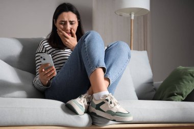 Evdeki koltukta cep telefonu kullanan depresif bir genç kadın.