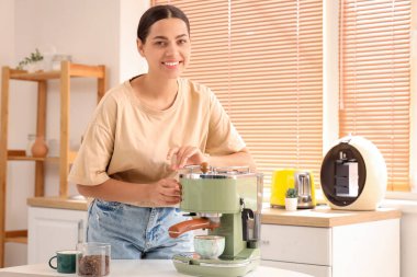 Mutfakta modern kahve makinesi olan güzel, genç ve mutlu bir kadın.