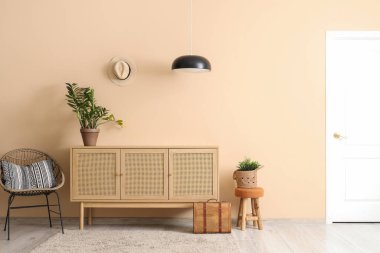 Ahşap dolabı, koltuğu ve bej duvarın yanında bitkileri olan şık bir oturma odası.