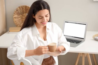 Bir fincan sıcak kahve ve dizüstü bilgisayarlı güzel bir kadın masada oturuyor.