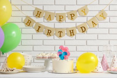 Beyaz tuğla duvara karşı doğum günü partisi için pasta, şeker ve dekor.