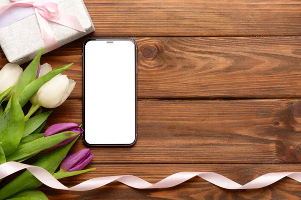 Modern cep telefonlu kompozisyon, güzel lale çiçekleri ve ahşap arka planda hediye kutusu.
