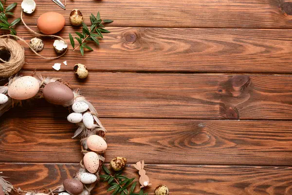 Ahşap arka planda yumurta ve tüylerle süslenmiş Paskalya çelengi.