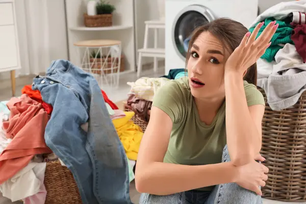 Çamaşır sepetiyle evde oturan yorgun genç kadın.