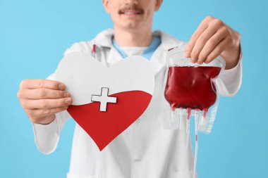 Kan nakli için erkek doktor ve mavi arka planda kağıt kalp, yakın plan.