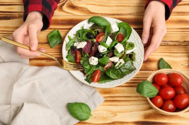 Sağlıklı sebze salatası, peçete ve ahşap arka planda malzemelerle dolu kadın elleri.