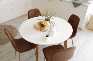 Mutfaktaki yemek masasında bir fincan kahve ve meyveli çaydanlık.