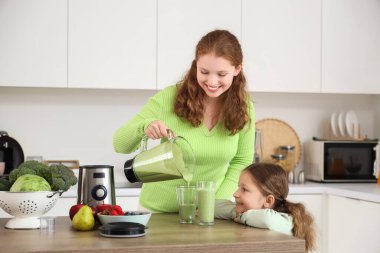 Anne ve küçük kızı mutfaktaki bardaklara smoothie dolduruyorlar.