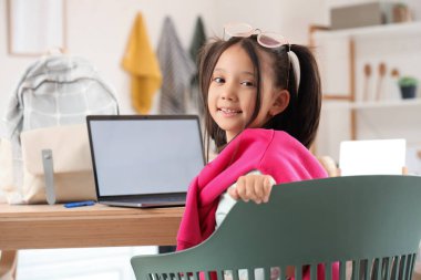 Bilgisayarlı küçük Asyalı kız mutfakta internetten ders çalışıyor.