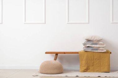 Beyaz duvarın yanında yastık yığını olan ahşap bir bank.