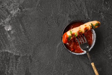 Lezzetli ızgara sosisli çatal ve siyah arka planda bir kase sos.