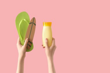 Parmak arası terlik, mini sörf tahtası ve pembe arka planda güneş kremi sürmüş kadın elleri.