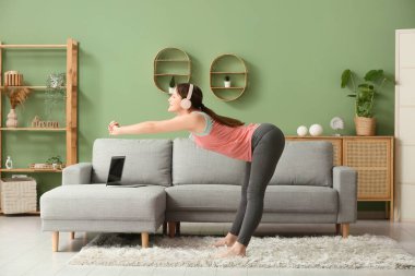 Kulaklıklı güzel bir kadın oturma odasında yoga yapıyor.