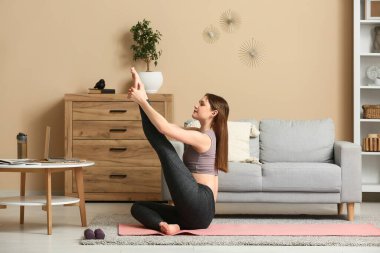 Güzel genç bir kadın oturma odasında yoga yapıyor.