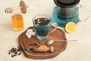 Çaydanlık, bir fincan kelebek, bezelye çiçeği çayı, şeker ve arka planda ahşap tepsi.