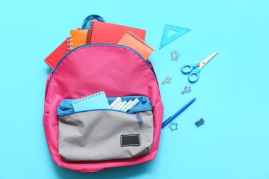 Mavi arka planda farklı kırtasiye malzemeleriyle modern okul sırt çantası.