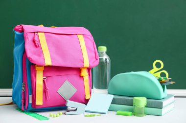 Okul çantasının içinde farklı kırtasiye malzemeleri ve beyaz masanın üzerinde bir şişe su vardı.