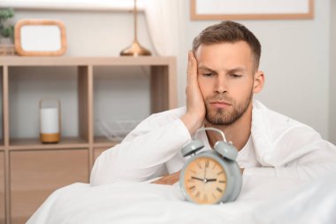 Genç adam ve çalar saat yatak odasında. Uykusuzluk kavramı