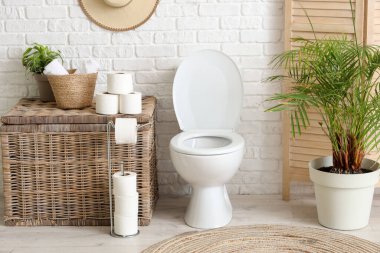 Tuvalet, çamaşır sepeti ve tuvalet odasındaki beyaz tuğla duvarın yanındaki katlı ekran.