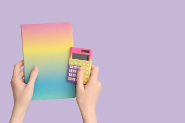Leylak arka planında defter ve hesap makinesi olan kadın elleri