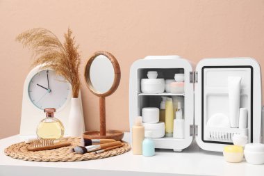 Kozmetik ürünleri, ayna ve saati olan küçük buzdolabı kahverengi duvara karşı.