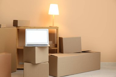 Boş dizüstü bilgisayar, taşınan kutular ve odada bej duvarın yanında parlayan lamba.