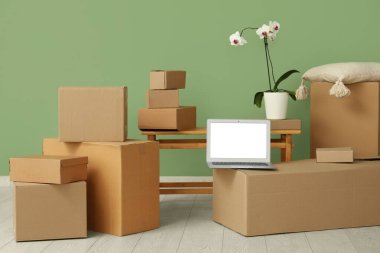 Boş dizüstü bilgisayar, taşınan kutular ve yeşil duvarın yanında orkide çiçeği.