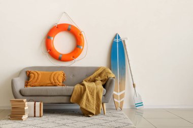 Oturma odasında minderli, ekose, sörf tahtalı, kürekli ve can simidi yüzüklü rahat bir kanepe.