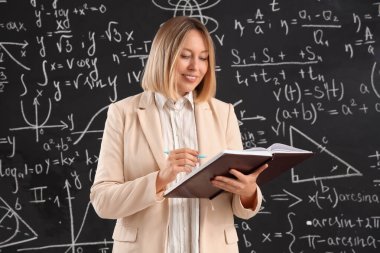 Sınıfta tahtaya yakın not defteri ve kalemi olan olgun bir matematik öğretmeni.
