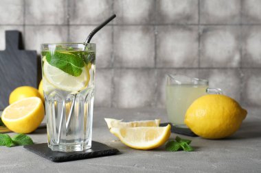Bir bardak taze limonata, nane ve gri masada meyveler.