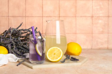 Bir bardak taze lavantalı limonata ve bej masa üzerinde çiçekler.