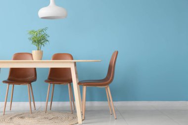 Sandalyeli yemek masası, mavi duvarlı ev bitkisi ve lamba.