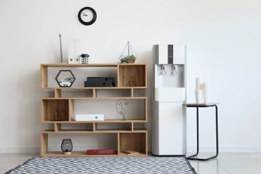 Ofisteki ışık duvarının yanındaki raflı ve masalı modern su soğutucusu.