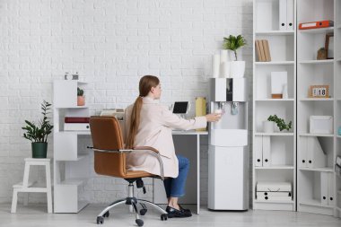 İş kadını ofisteki soğutucudan su dolduruyor.