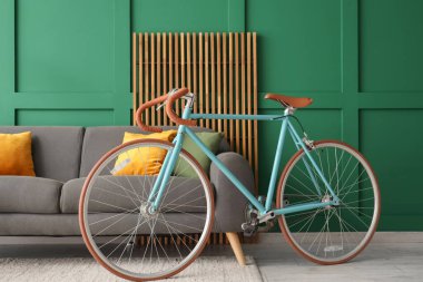 Oturma odasındaki yeşil duvarın yanında rahat bir kanepe, ekran ve bisiklet.