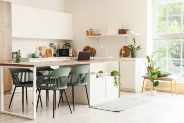 Beyaz duvarın yanında masalı, sandalyeli ve tezgahlı bir yemek odası.