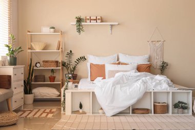 Büyük konforlu yatak, ev bitkileri, çekmeceler ve yatak odasının içindeki raf üniteleri.