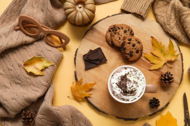 Sonbahar kompozisyonu bir fincan kakao, kazak, ahşap tepsi ve sarı arka planda kurabiyeler.