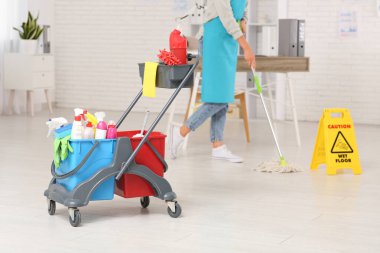 Tramvay ve uyarı levhası olan hademe ofiste yerleri paspaslıyor.