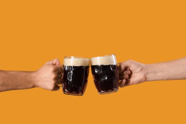 Turuncu arka planda soğuk bira bardakları olan erkek elleri. Ekim Festivali Kutlaması