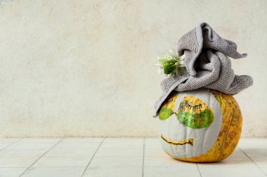 Çizilmiş yüzlü balkabağı, kil maske, göz altı bantları, havlu ve çiçekler ışık duvarının yanındaki fayans masasında.