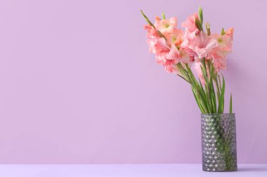 Leylak arka planında bir buket güzel gladiolus çiçeği olan cam vazo.