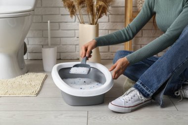 Tuvaletteki kedi için kepçe kepçesi temizleyen kadın.