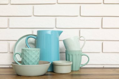 Bardaklar, kaseler ve sürahiler beyaz tuğla duvarın yanındaki ahşap masada.