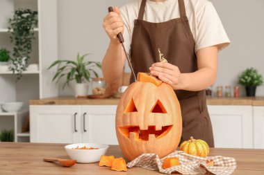 Mutfakta tezgahta balkabağı oyan bir kadın ve bir kase tohum.